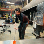 A demo duck team member at a glass blowing event rolling the glass